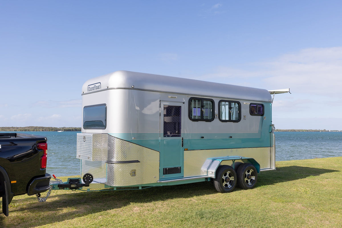 Silver and teal EuroFloat float hitched to a black ute on grass beside the water