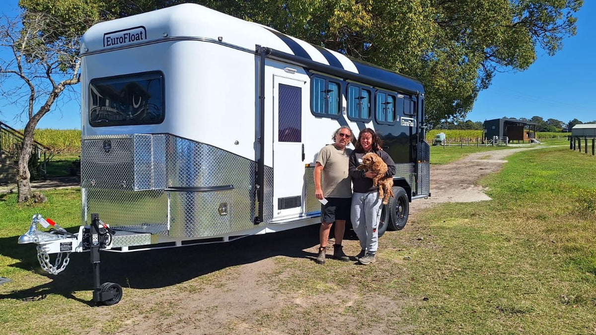 Couple holding their dog beside their new white and black EuroFloat horse float on a farm track